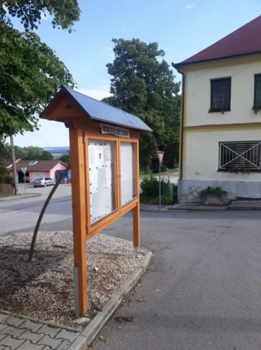 samostatně stojící dřevěná úřední deska se sedlouvou střechou.